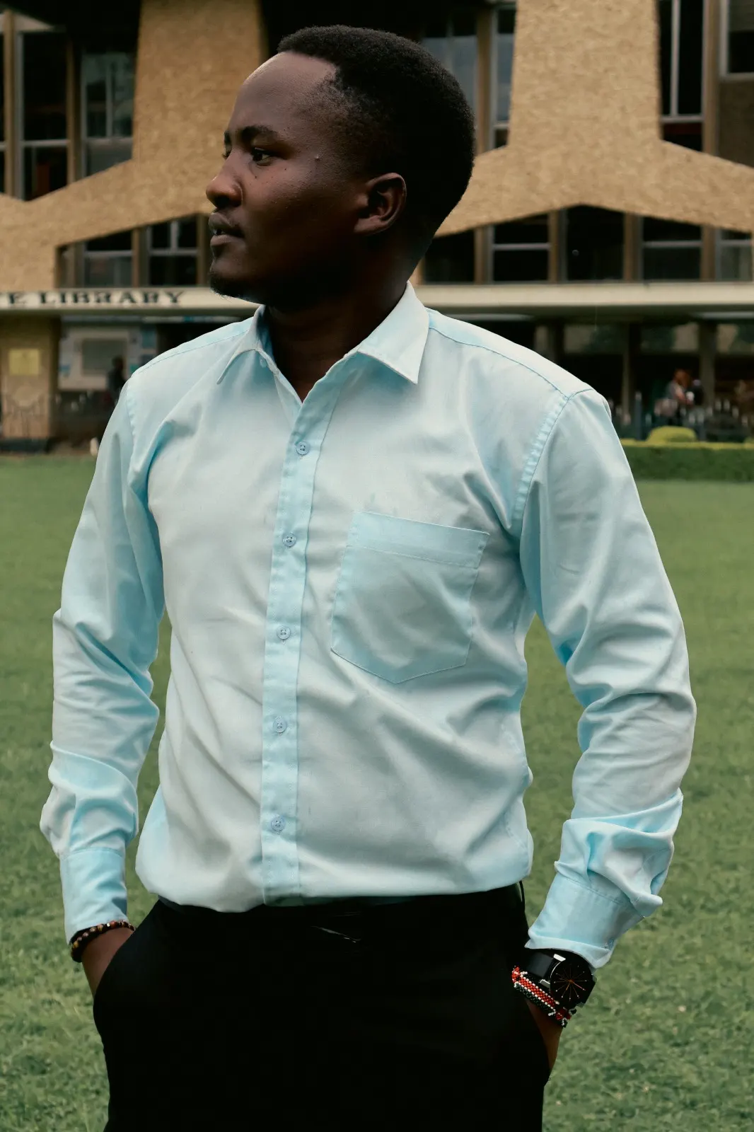 Ian Asena in a pale blue shirt, photographed in profile before a university library