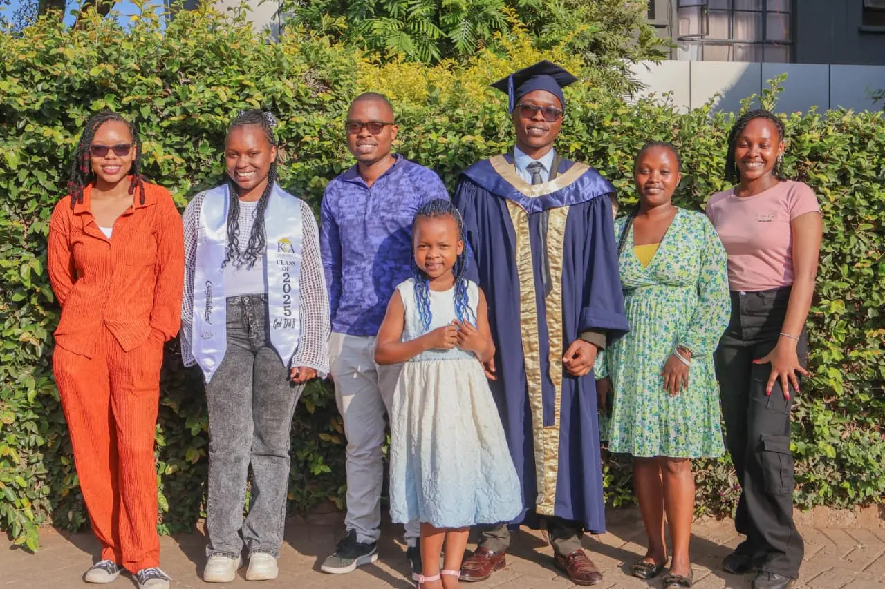 The graduate in his gown flanked by friends in bright colours, one wearing a Class of 2025 sash